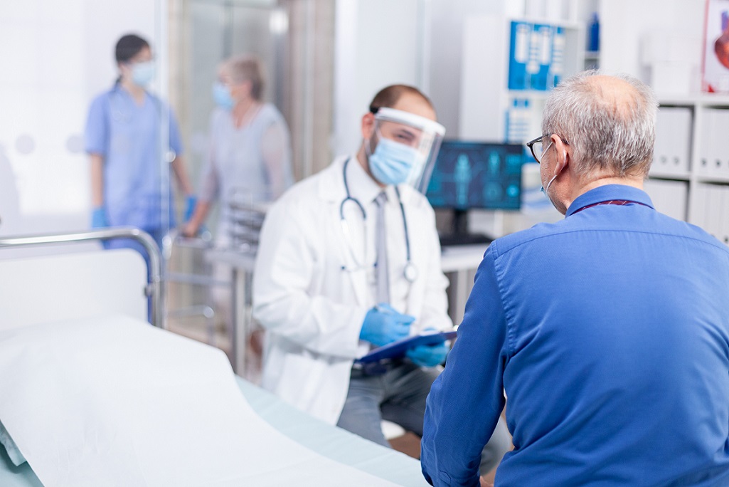 Old patient listening doctor diagnosis while wearing protective mask against coronavirus outbreak in hospital examination room. Modern private clinic . Practitioner physician appointment.